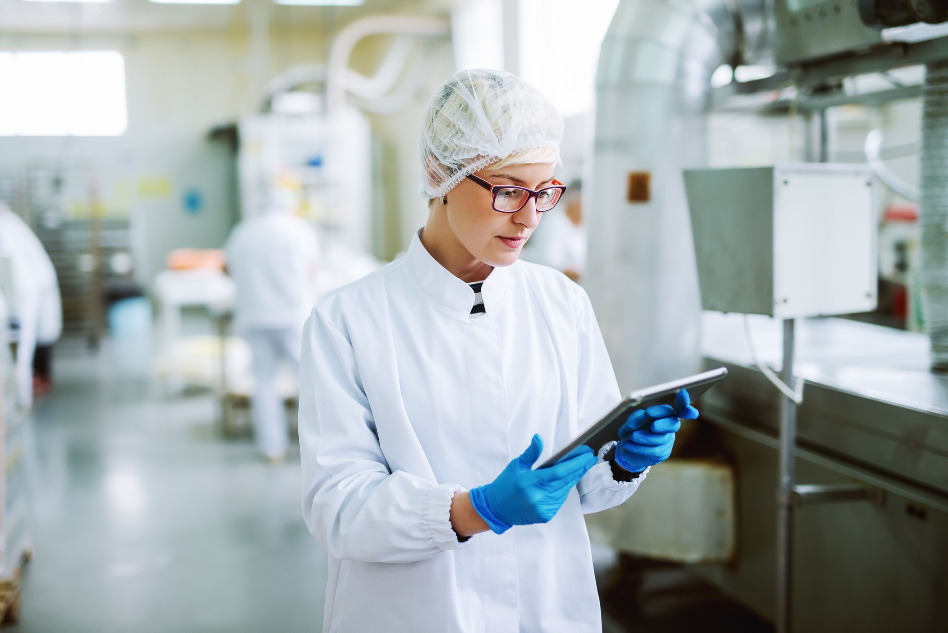 Female worker using tablet for controling products while standing in food factory.